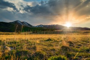 green grass field near mountain under cloudy sky during daytime